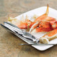 Crab legs on a white plate with a pair of metal crab Crackers on a stone surface