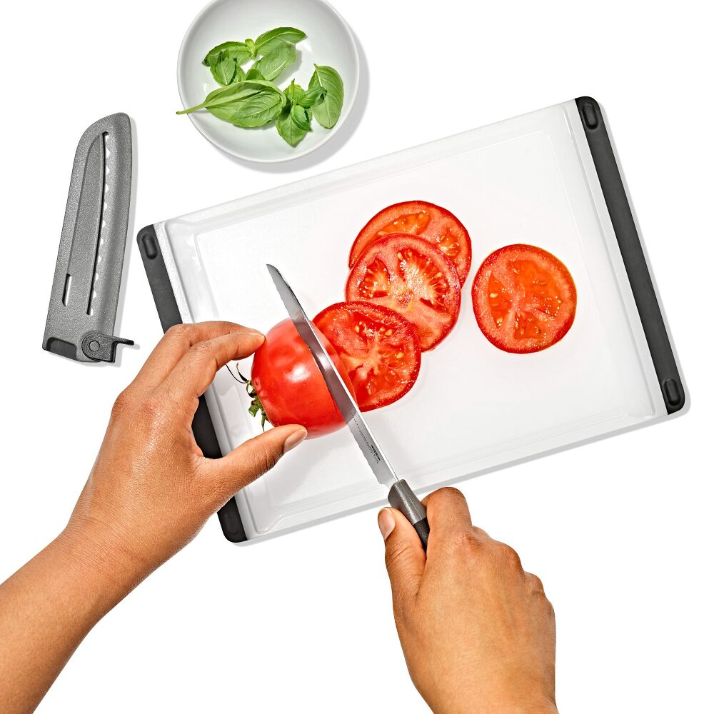 and using a knife to cut tomatoes on a white cutting board. 