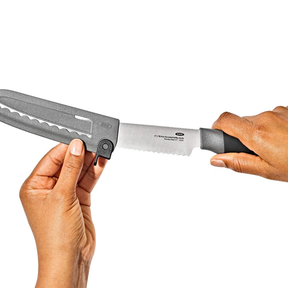 Hand putting a serrated knife into a black sheath. 