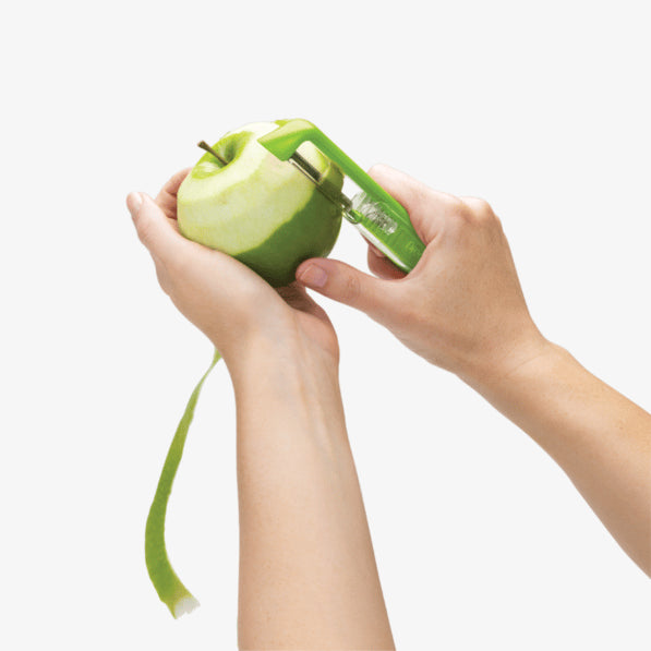 Person using a green apple peeler to remove the skin of a green apple on a white background.