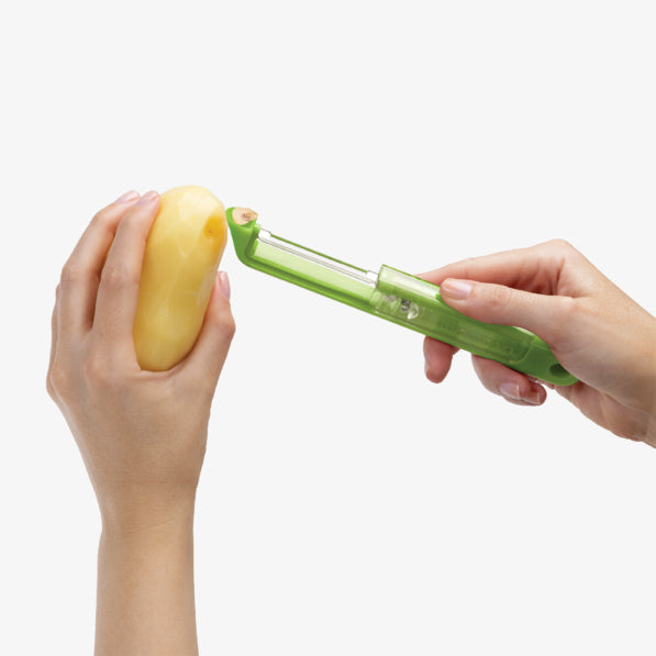 Person using a green potato peeler to peel a yellow potato on a white background.