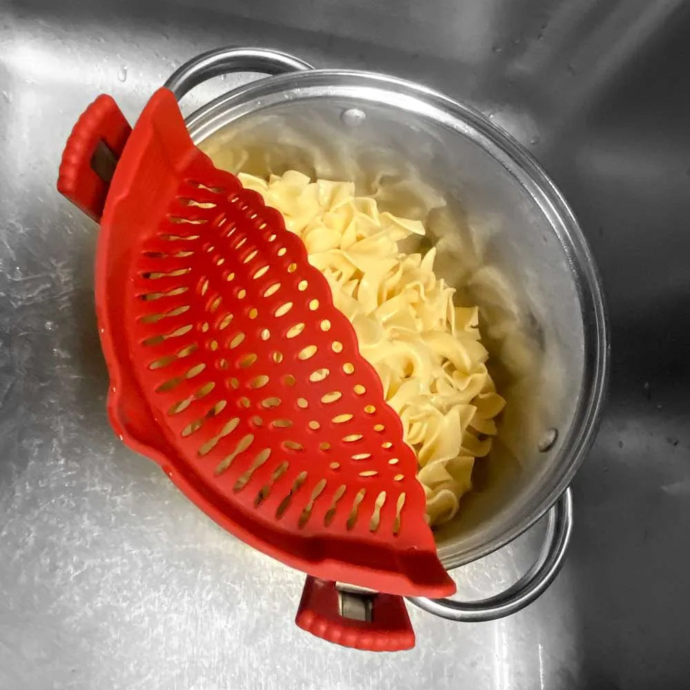 Red silicone strainer over a pot of cooked pasta in a sink.