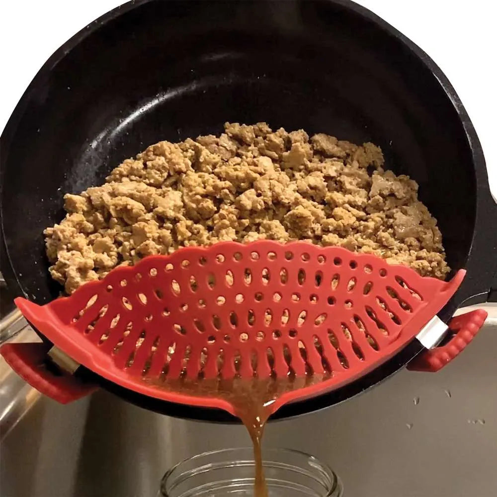 A red silicone leaf-shaped strainer held over a black pan, draining a brown liquid from cooked ground meat.