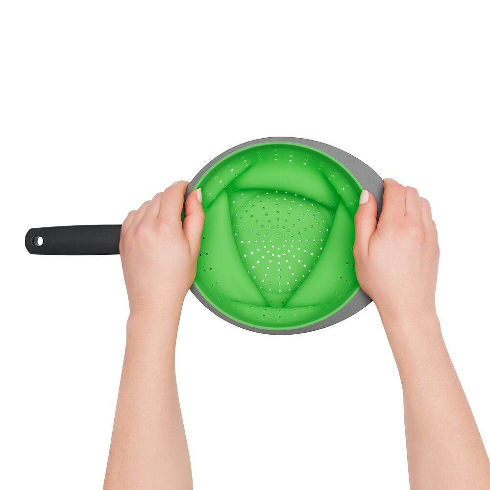 Hands attempting to collapse a green silicone strainer. 