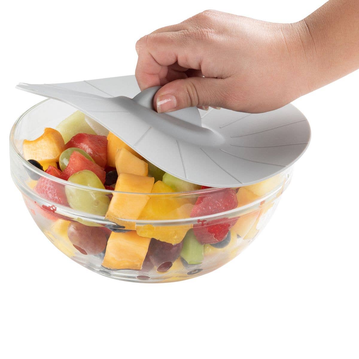 Hand placing a silicone lid on a glass bowl filled with fruit.