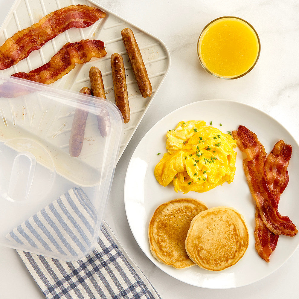 Breakfast setting with pancakes, eggs, bacon, and sausages on a white plate, with a side of orange juice.