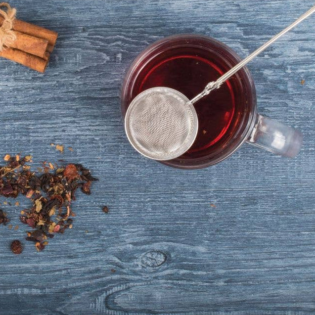 Tea cup with a strainer, cinnamon sticks, and dried herbs on a wooden surface