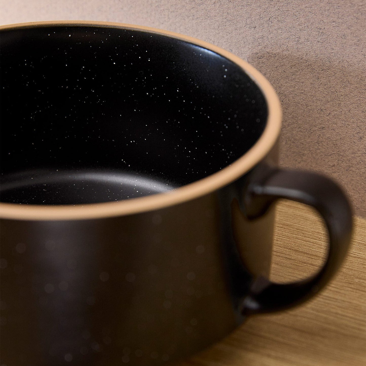 Black ceramic mug with speckled interior on a wooden surface