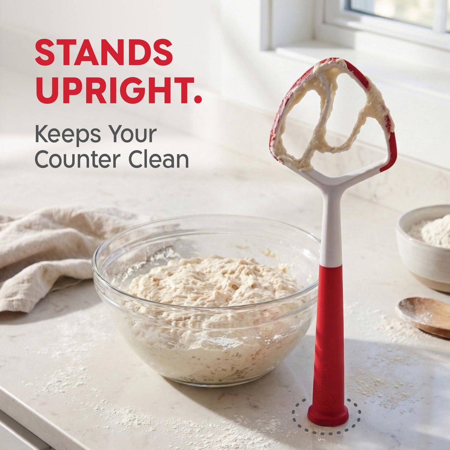 Red kitchen tool next to a bowl of dough on a light surface with text about it standing upright.