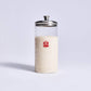 Clear glass Sourdough Storage Crock with a metal lid and red logo on a light gray background