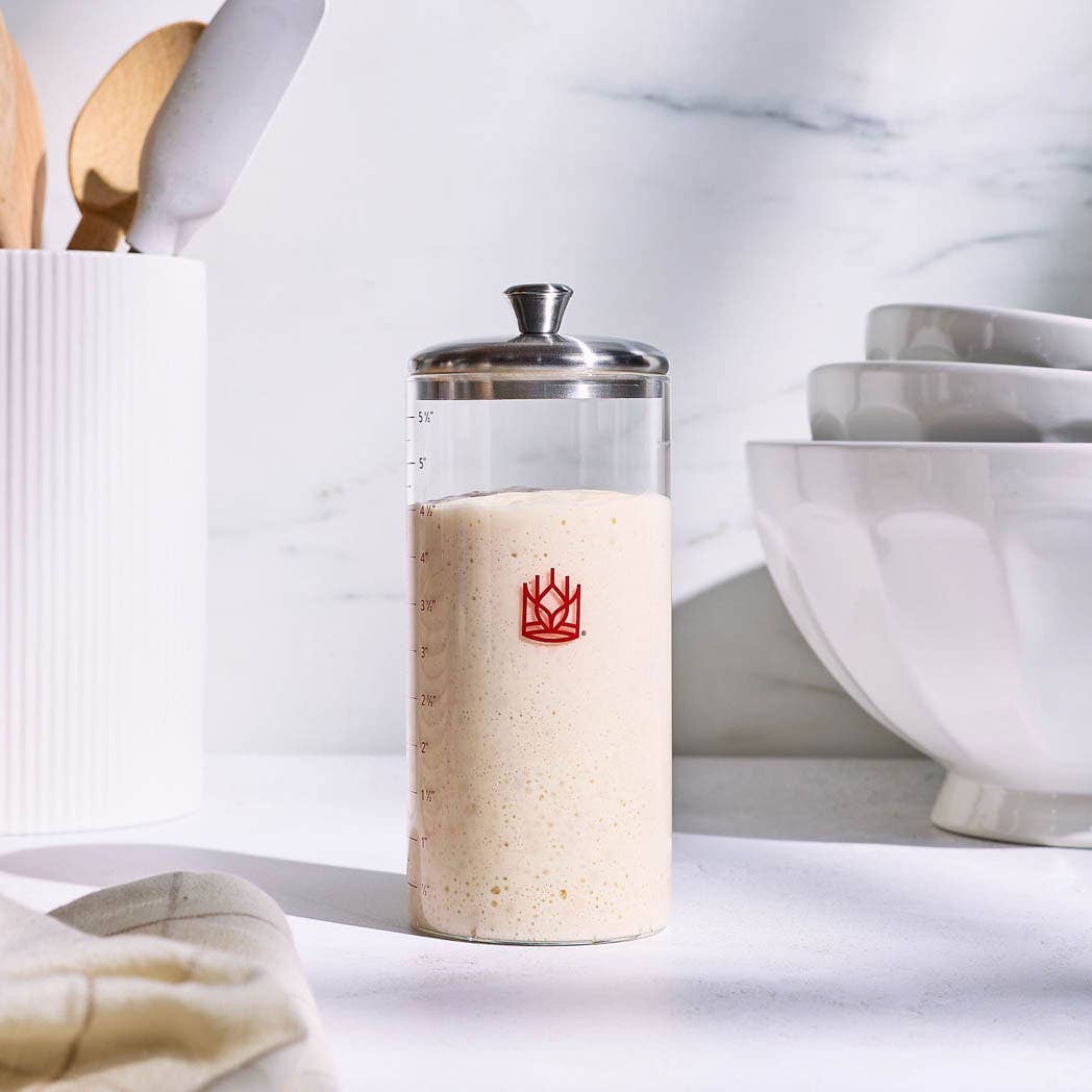 Glass Sourdough Storage Crock with a  red logo on a marble surface