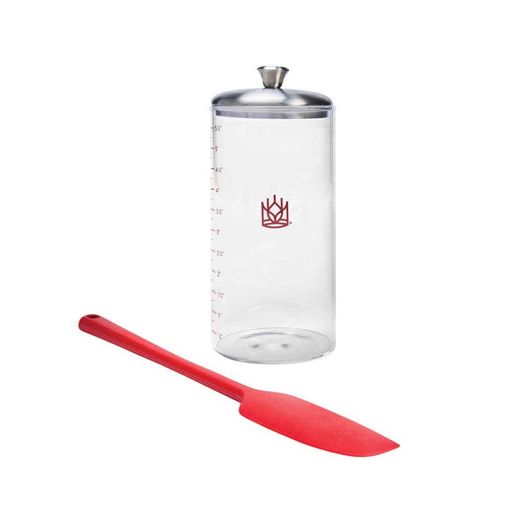 Clear Sourdough Storage Crock with silver lid and red spatula on a white background