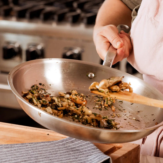 A stainless steel frying pan with cooked herbs being held in a kitchen.