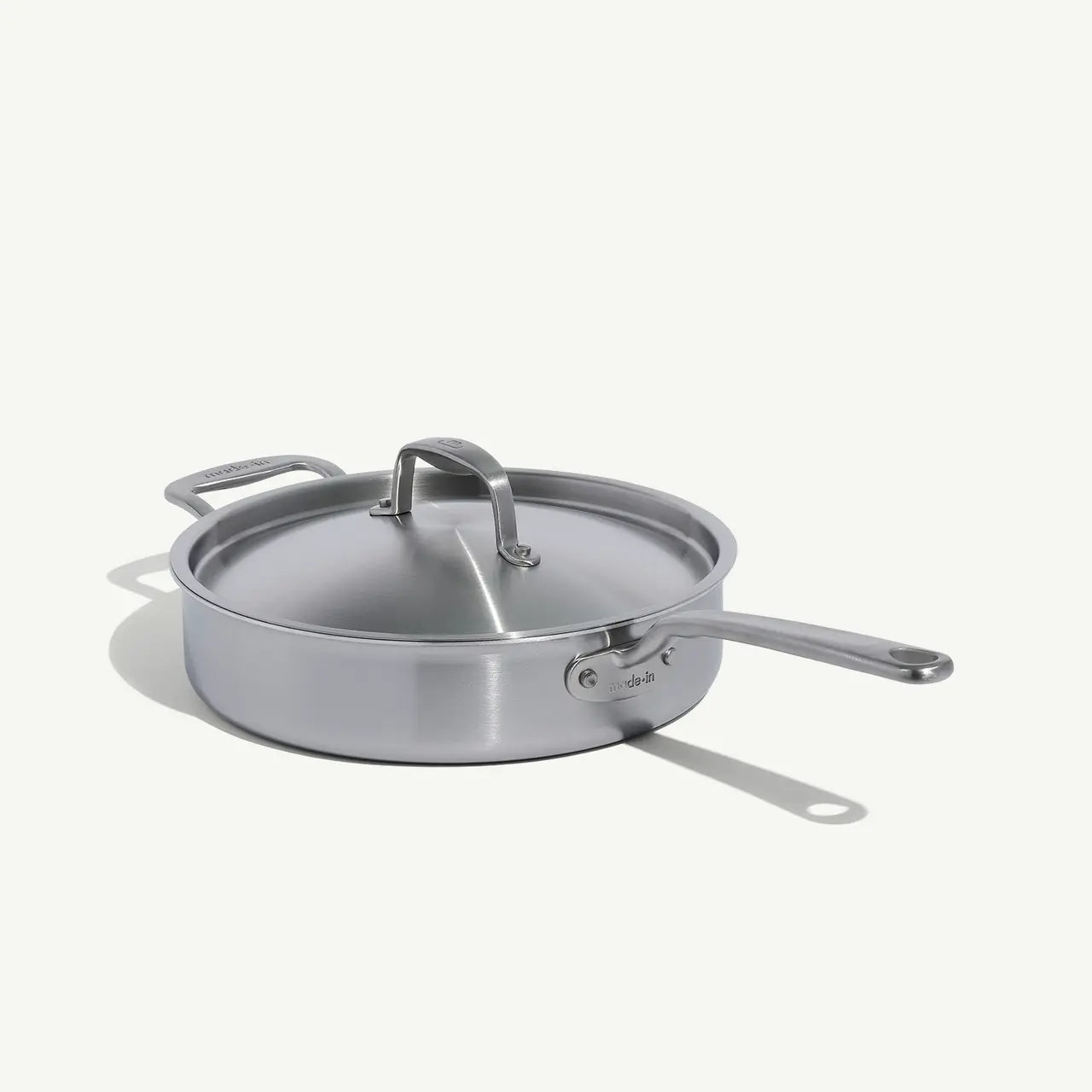 A stainless steel sauté pan with a lid and stay-cool handle, on a white background.