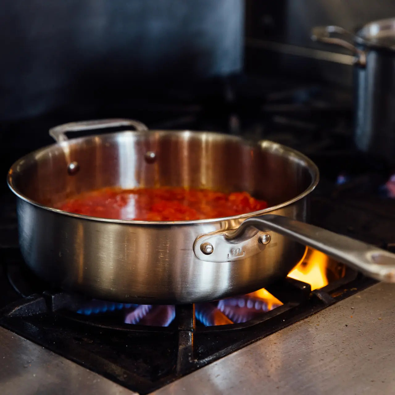 A stainless steel sauté pan cooking red sauce on a kitchen stovetop. 