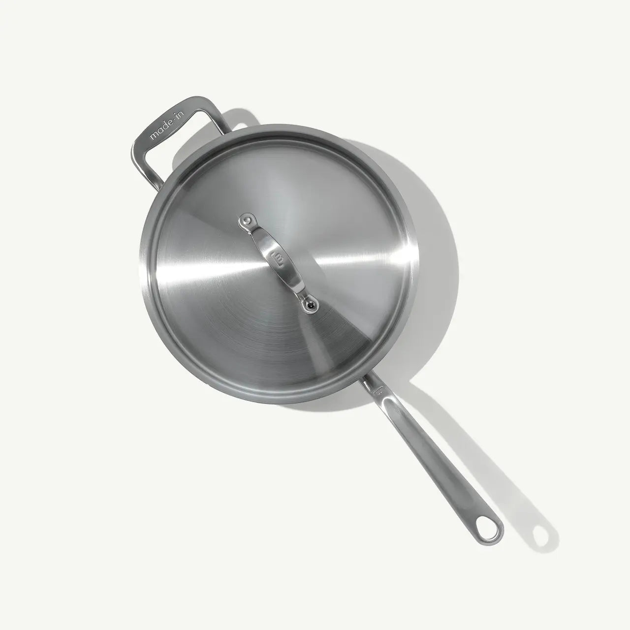 A stainless steel sauté pan with a lid and stay-cool handle, on a white background.