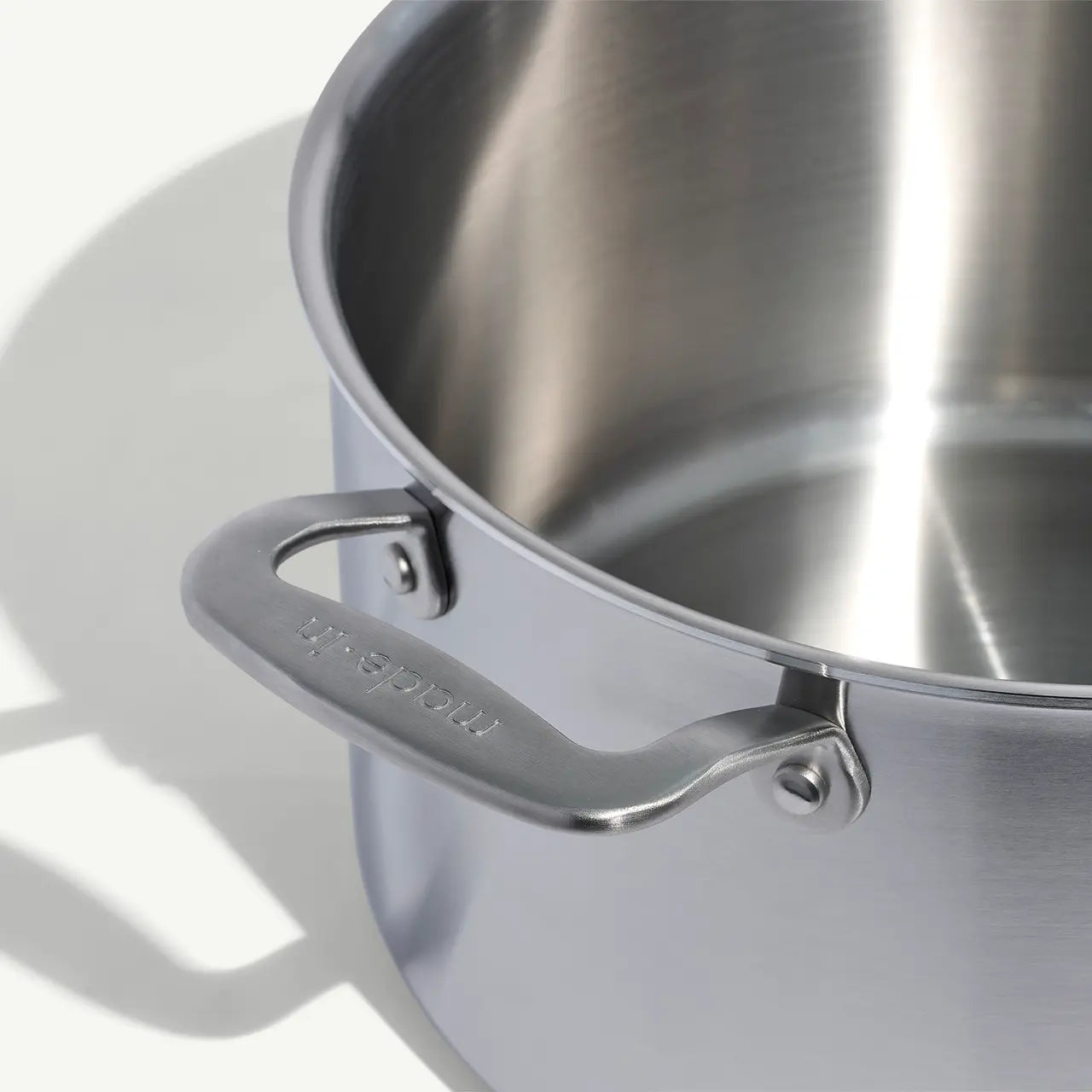 A silver stainless clad stock pot with lid, featuring two handles and a fitted lid, on a white background.