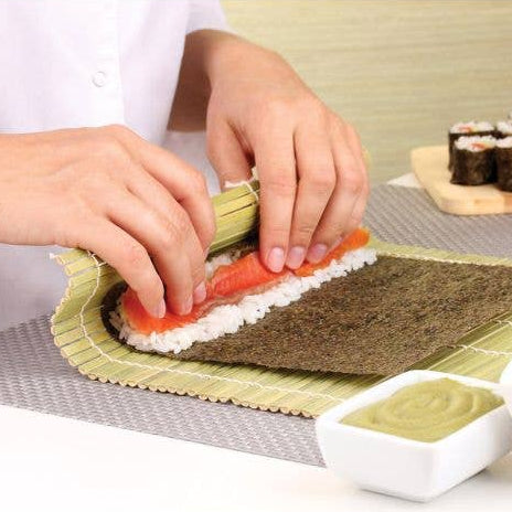Person making sushi with a bamboo mat and ingredients on a table.