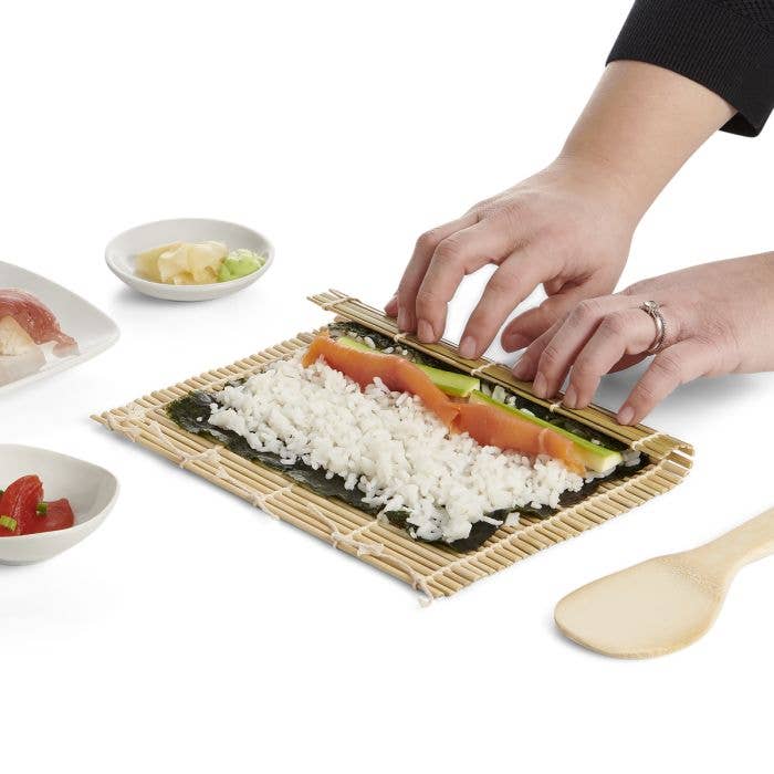 Person making sushi with bamboo mat on a white background