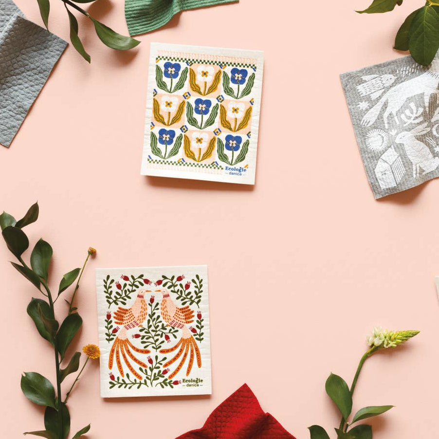 Four decorative Swedish dishcloths with animal illustrations on a pink background with green leaves.