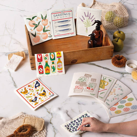 Collection of illustrated swedish dishcloths on a marble surface with a wooden tray.