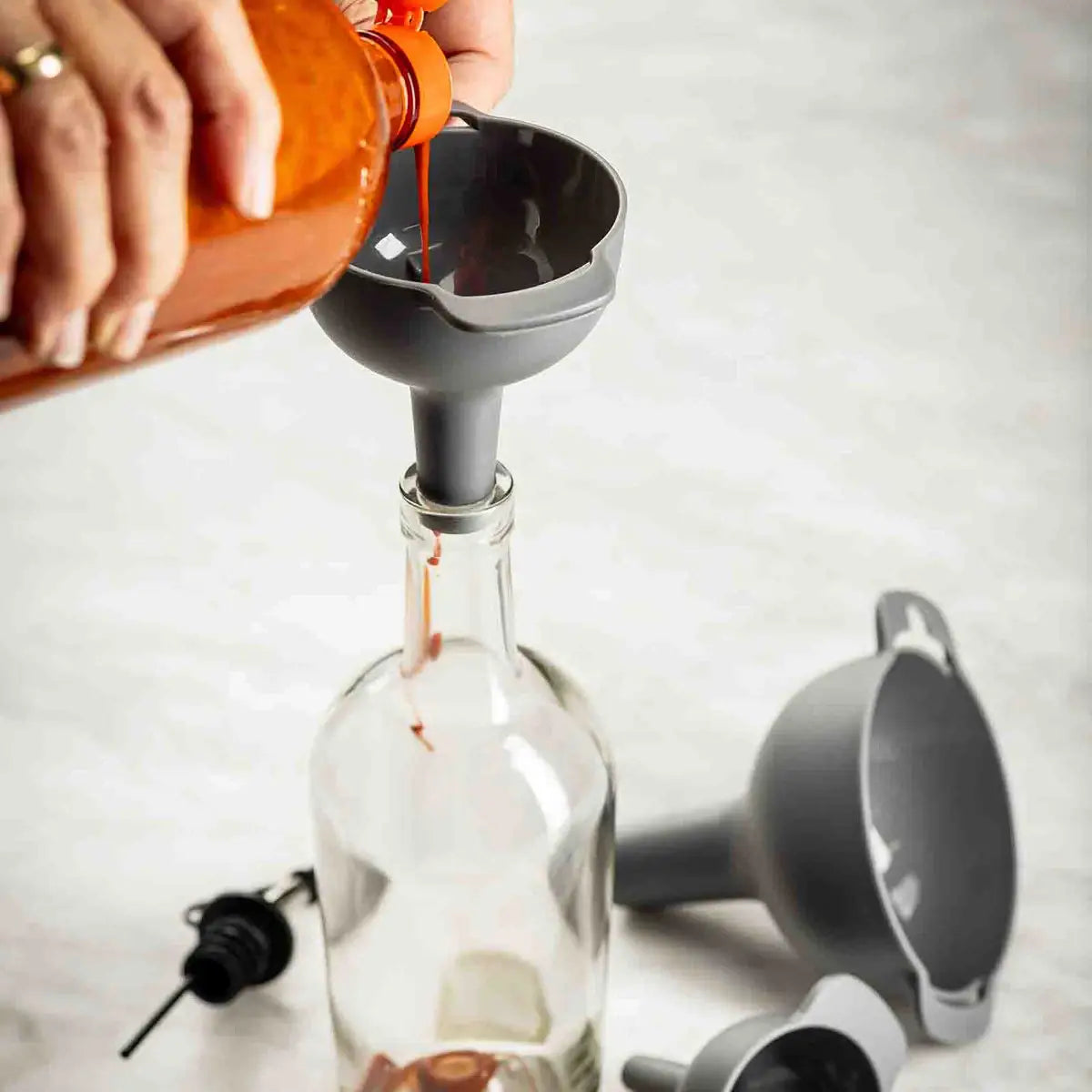 Person pouring liquid from a bottle into a glass bottle using a funnel.