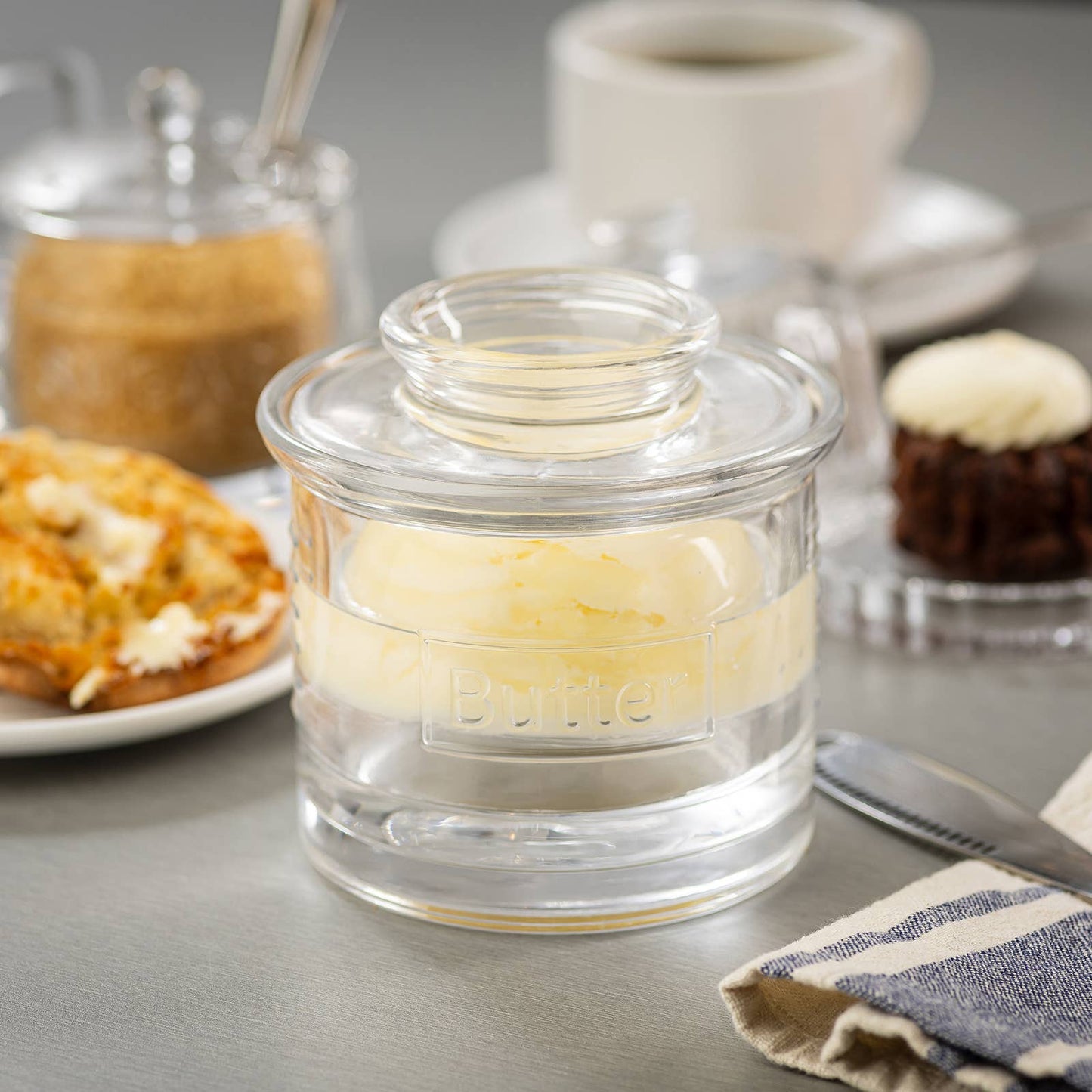 Glass jar with butter on a table with pastries and coffee in the background