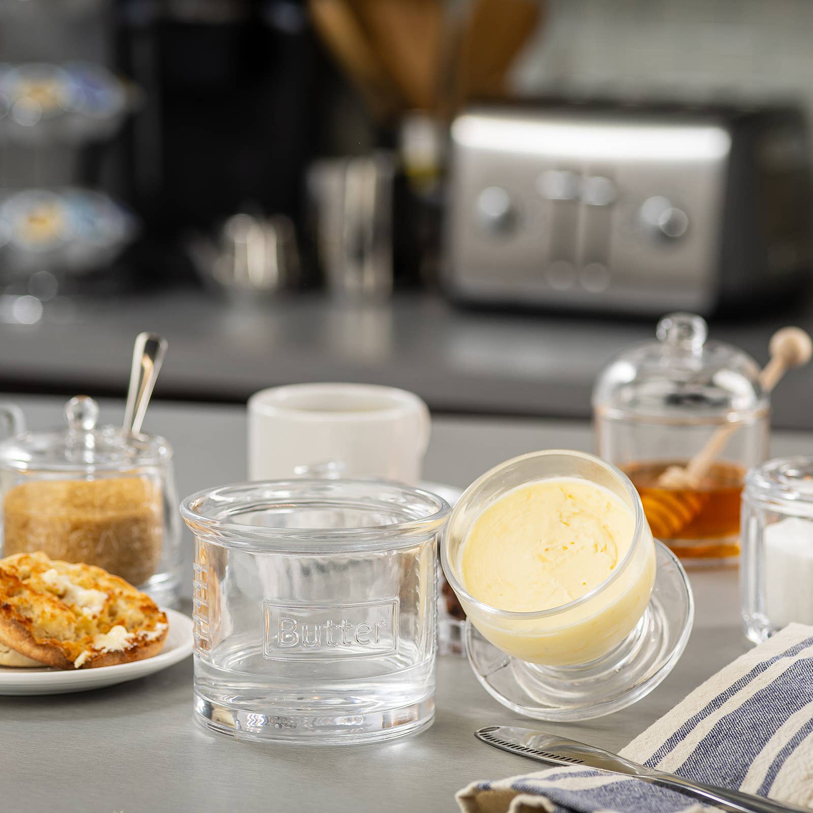 Butter dish with a knife on a kitchen counter, featuring a coffee maker in the background.