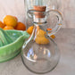 Clear glass carafe with cork stopper on a countertop with fruits in the background