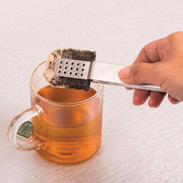 Tea bag being removed from a glass of tea with a metal tea infuser.
