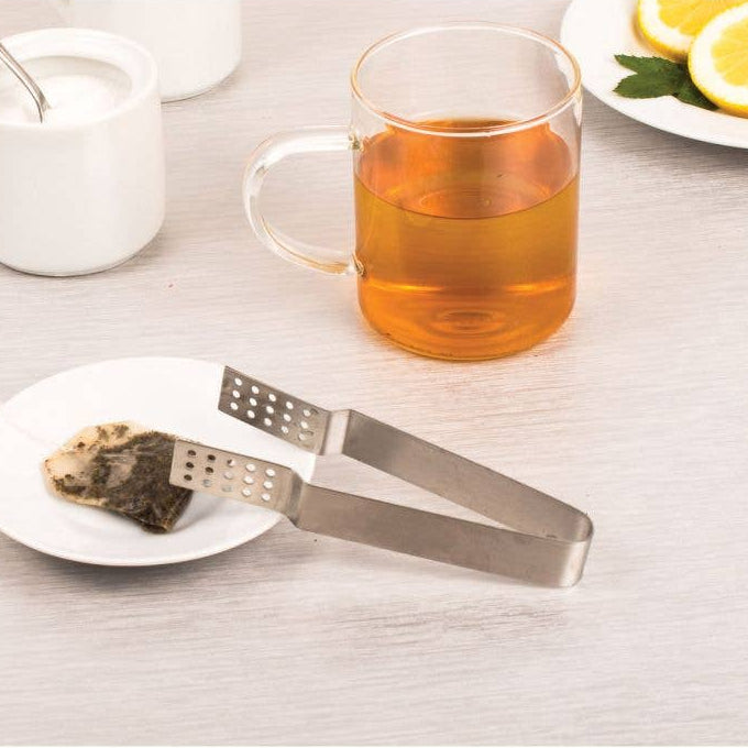 Tea tongs with a tea bag and mug of tea on a table