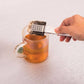 Tea bag being removed from a glass of tea with a metal tea infuser.