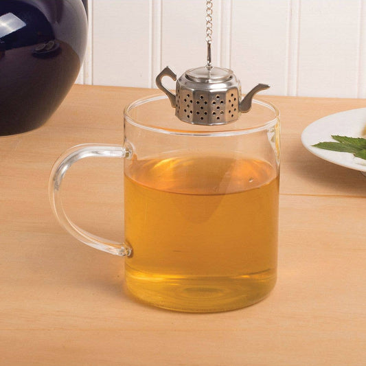 Clear glass mug with tea and a metal teapot on a wooden table