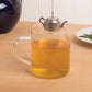 Clear glass mug with tea and a metal teapot on a wooden table