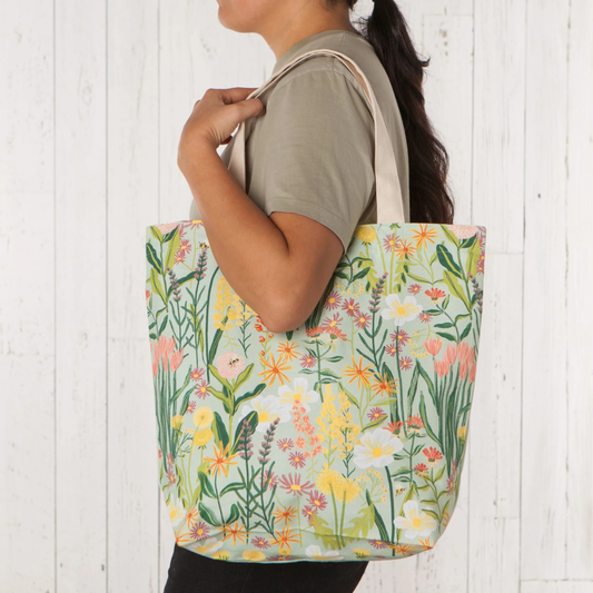 Person holding a tote bag with floral pattern against a white wooden background