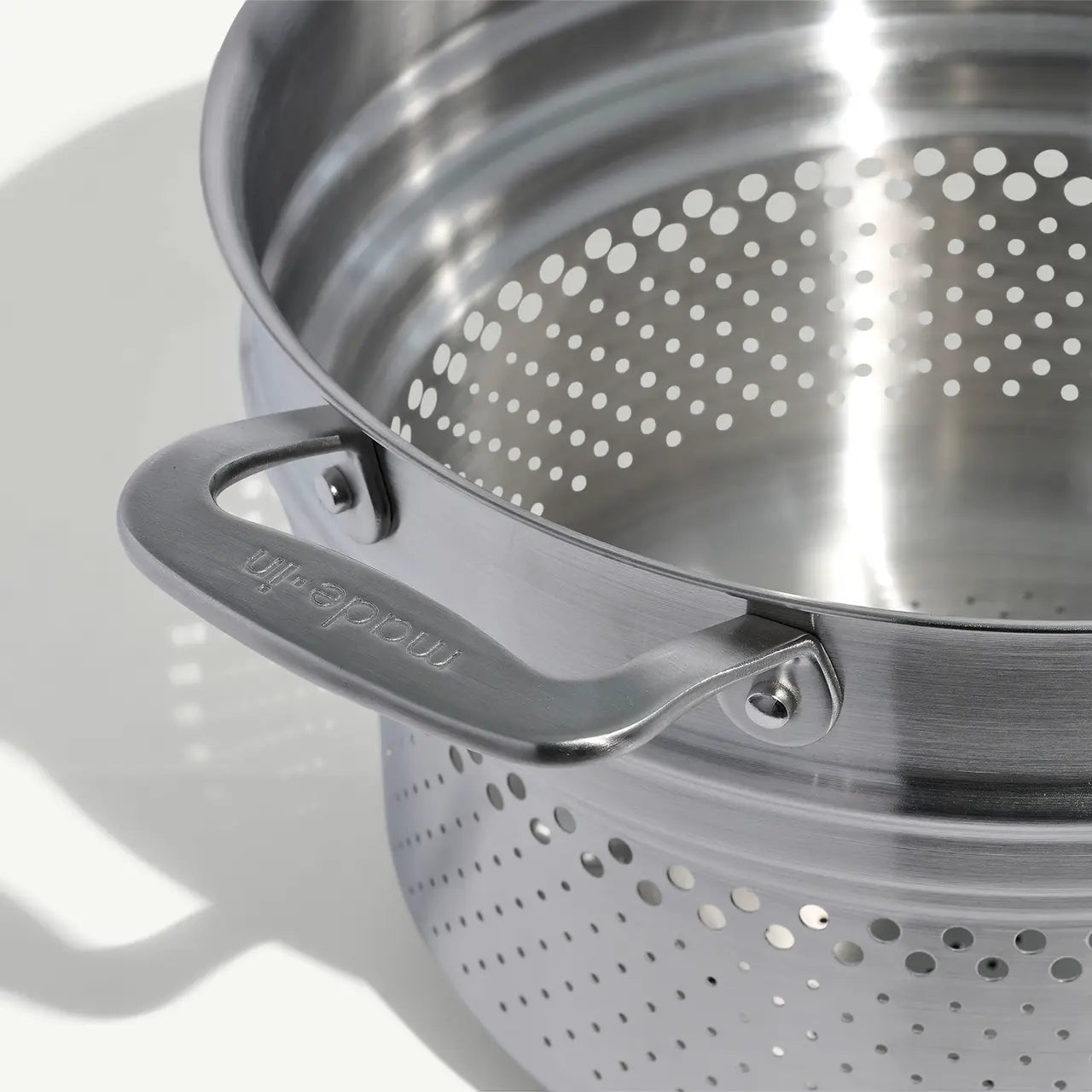 A stainless steel pasta insert with slotted holes designed to fit into a stock pot for cooking pasta on a white background.