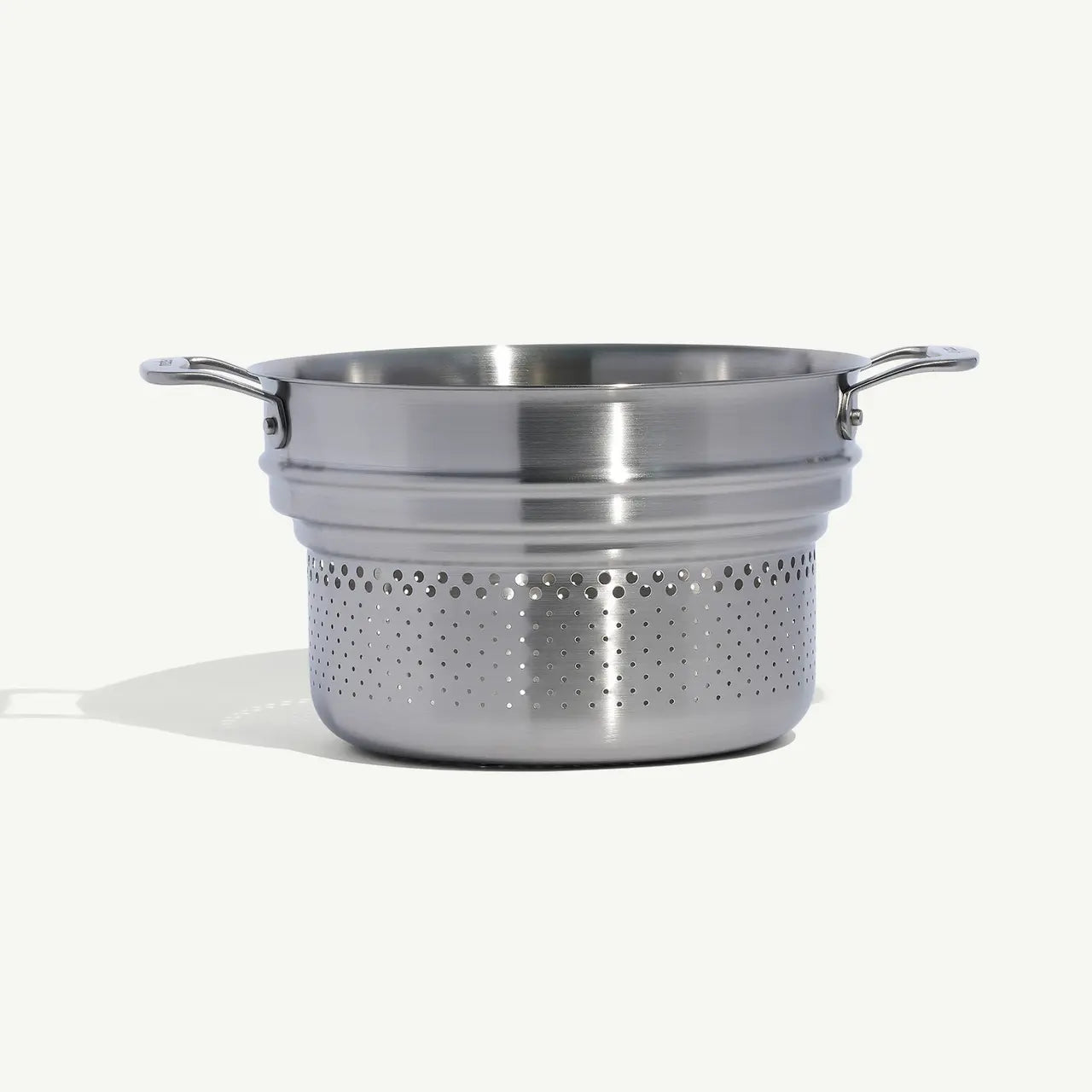 A stainless steel pasta insert with slotted holes designed to fit into a stock pot for cooking pasta on a white background.