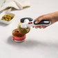Hand using a can opener on a can of smoked salmon with olives in the background.