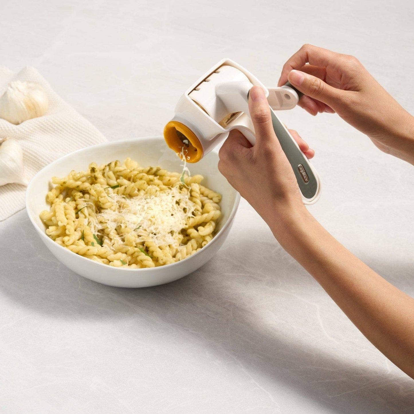 Person sprinkling cheese over a bowl of pasta on a light surface.