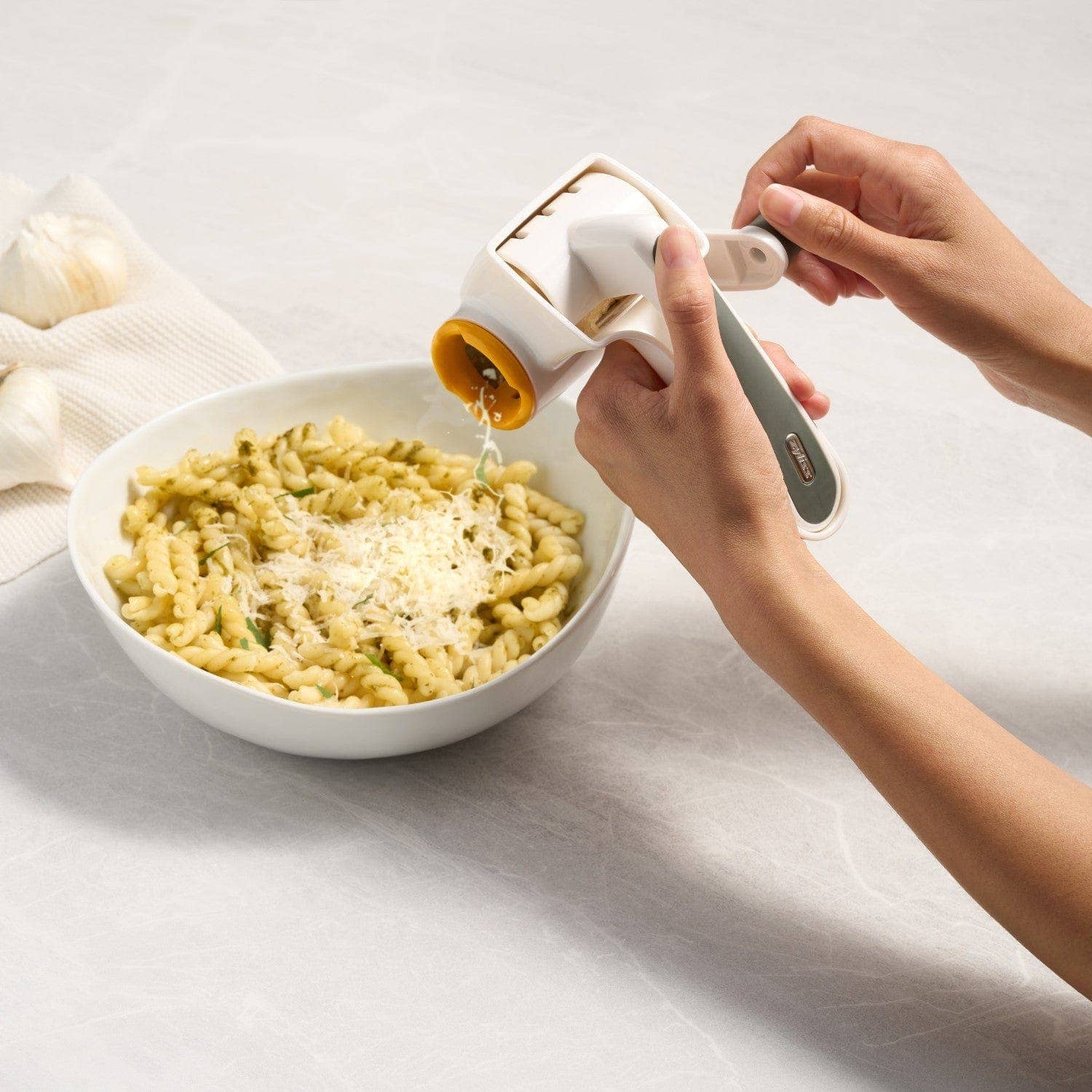 Person sprinkling cheese over a bowl of pasta on a light surface.