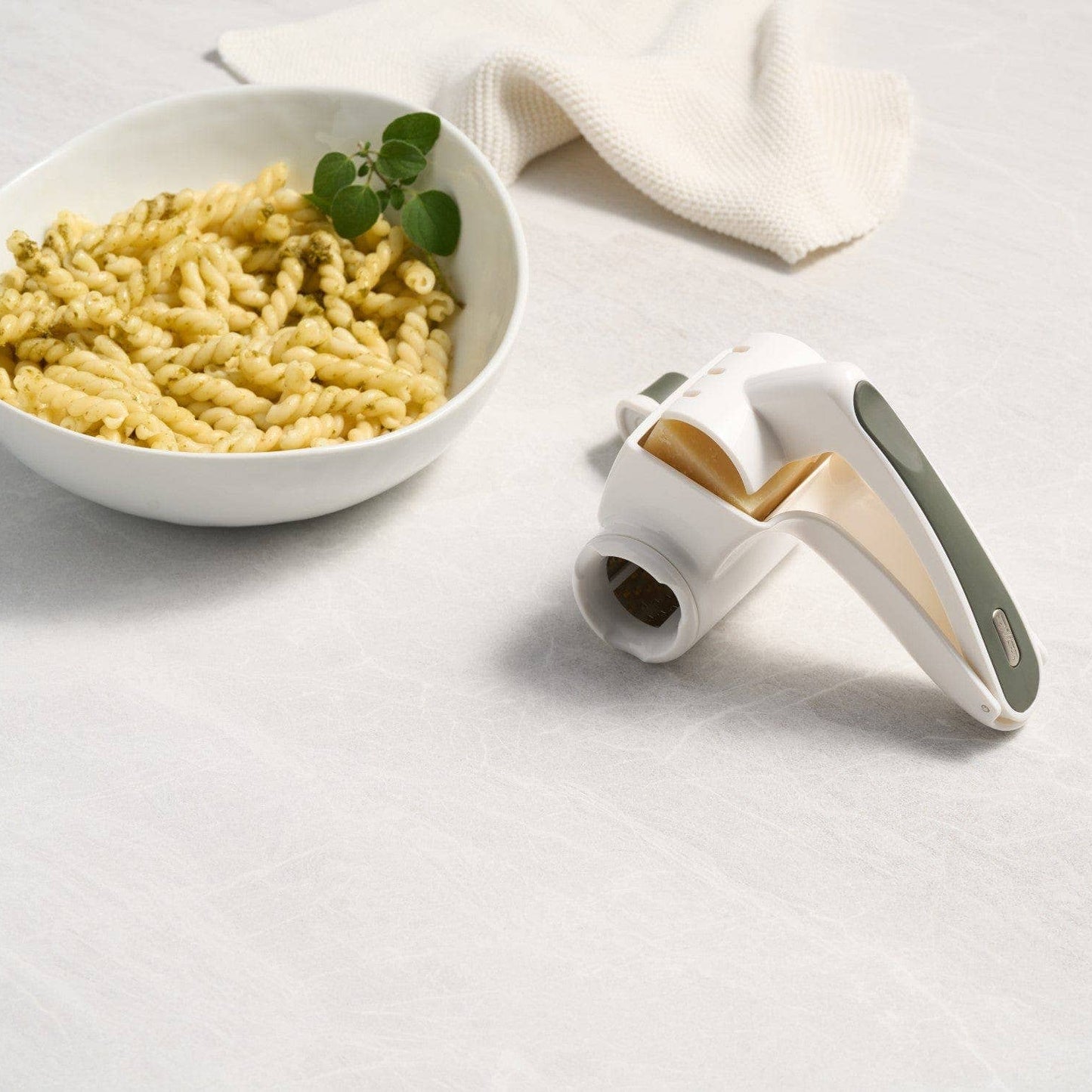 Pasta maker next to a bowl of pasta on a light surface