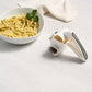 Pasta maker next to a bowl of pasta on a light surface