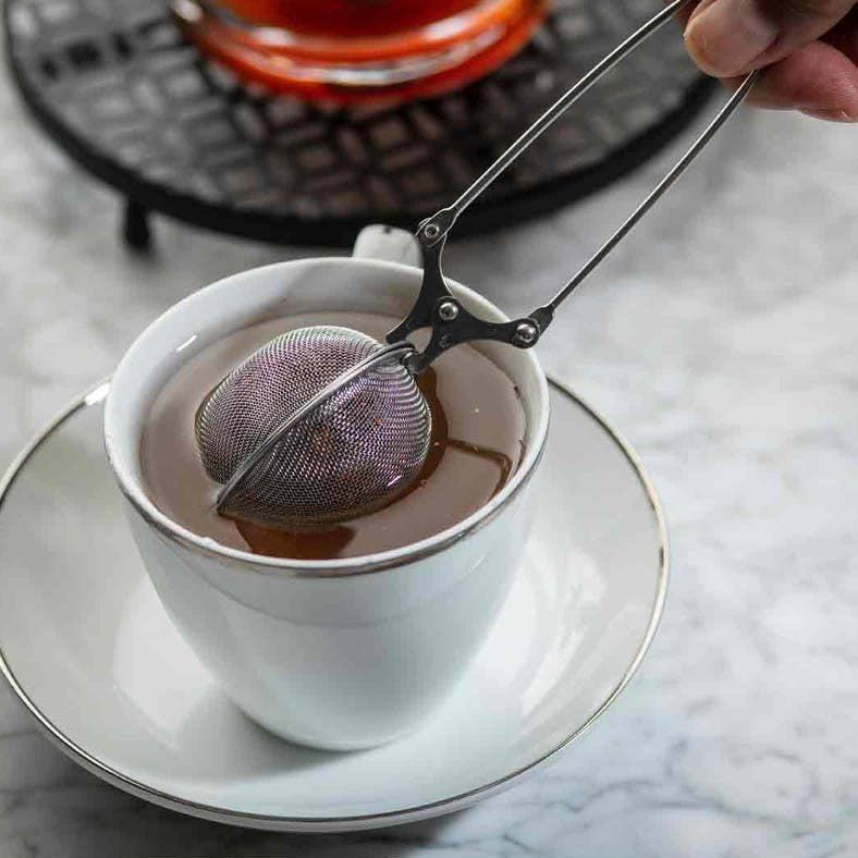 Person using a tea infuser in a white cup on a marble surface