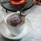 Person using a tea infuser in a white cup on a marble surface