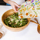 Person preparing a salad with a colorful towel featuring fruits and vegetables on a white table.