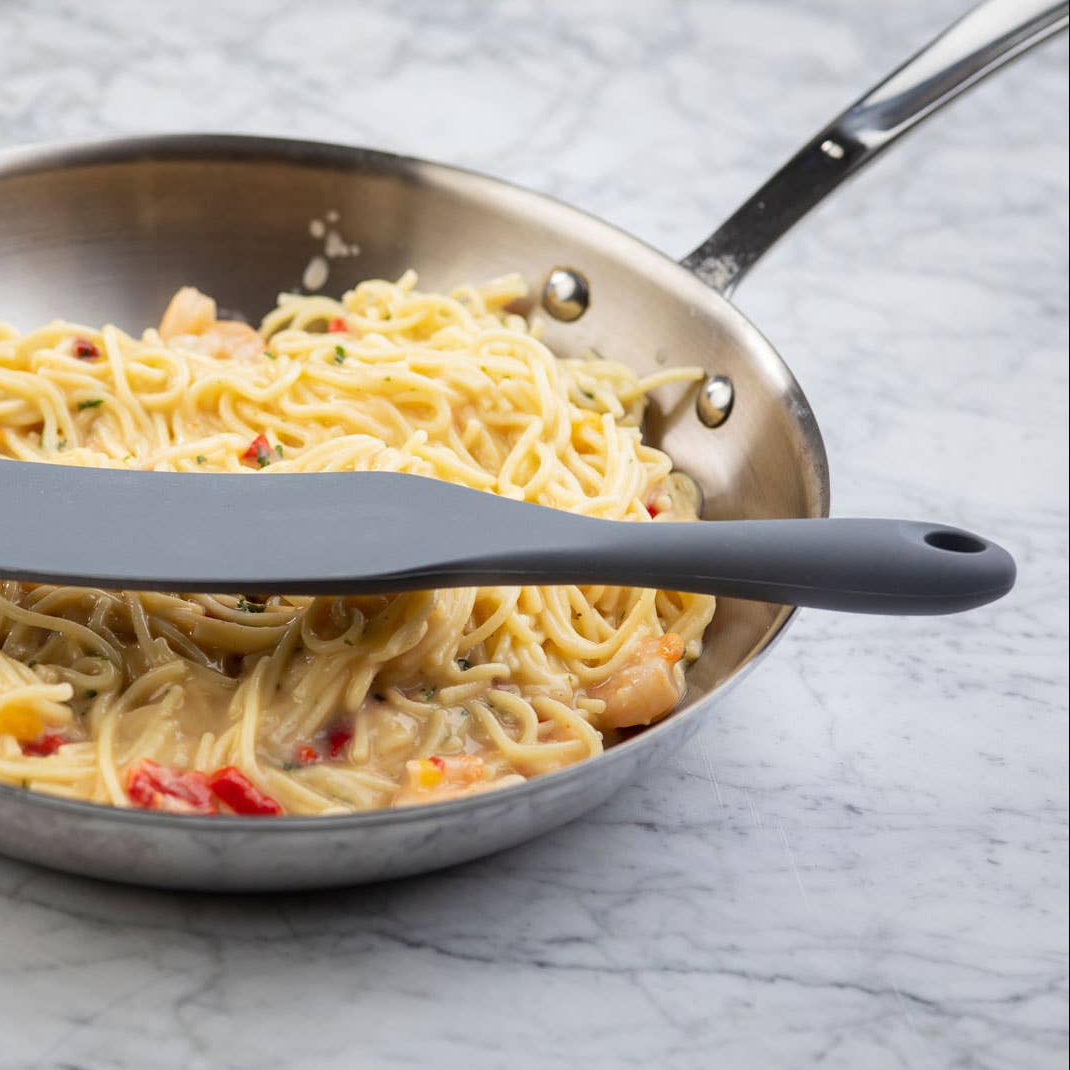 Frying pan with spaghetti and a black spatula on a marble surface