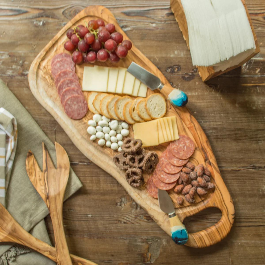 olive wood charcuterie board on a table with meats, cheeses, grapes and crackers