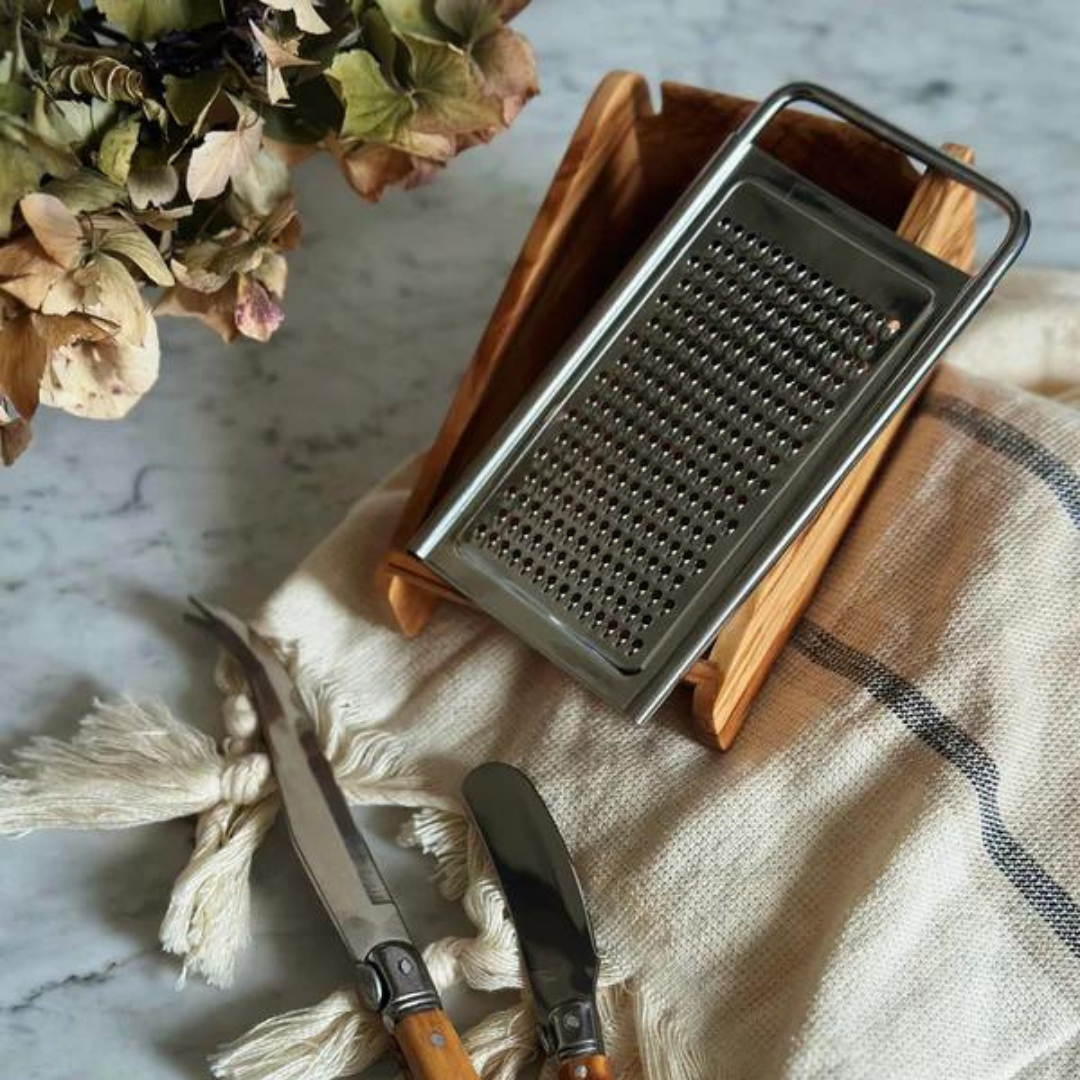 olive wood cheese grater on counter with towel and utensils 