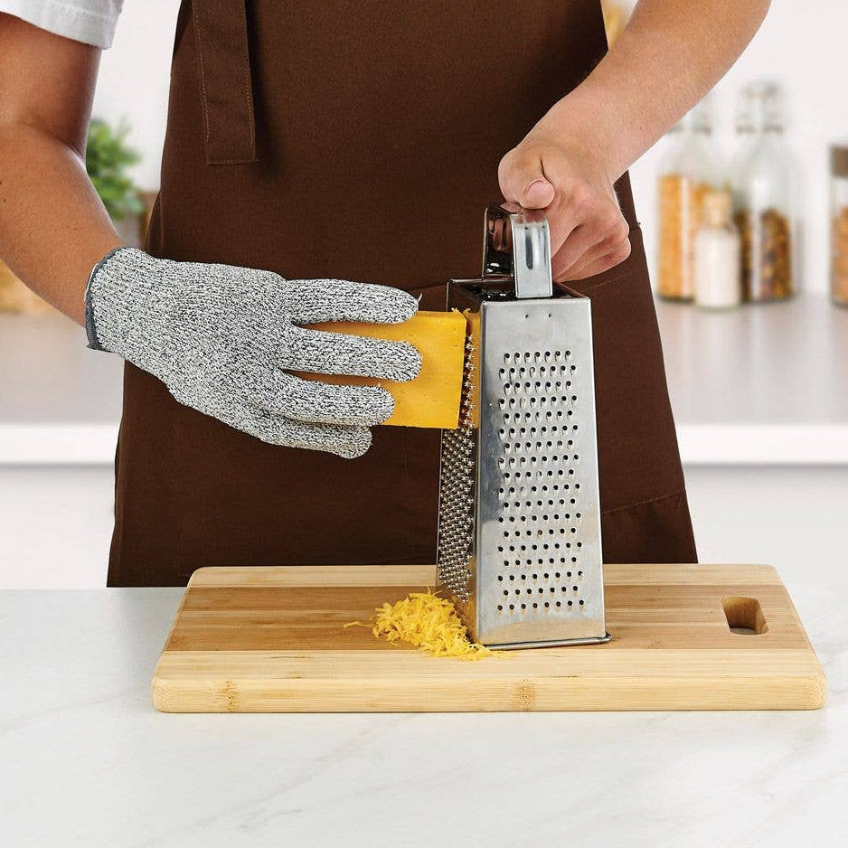 Person grating cheese with a box grater on a wooden cutting board in a kitchen.