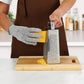 Person grating cheese with a box grater on a wooden cutting board in a kitchen.